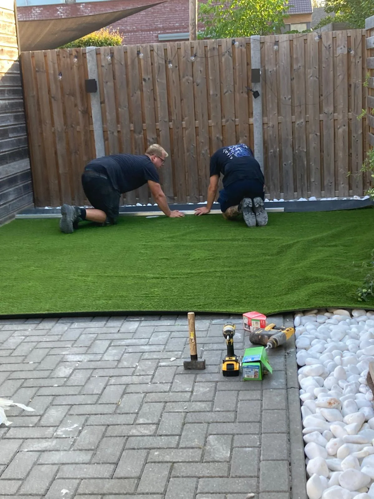 Twee tuinmannen leggen kunstgras in een kleine achtertuin